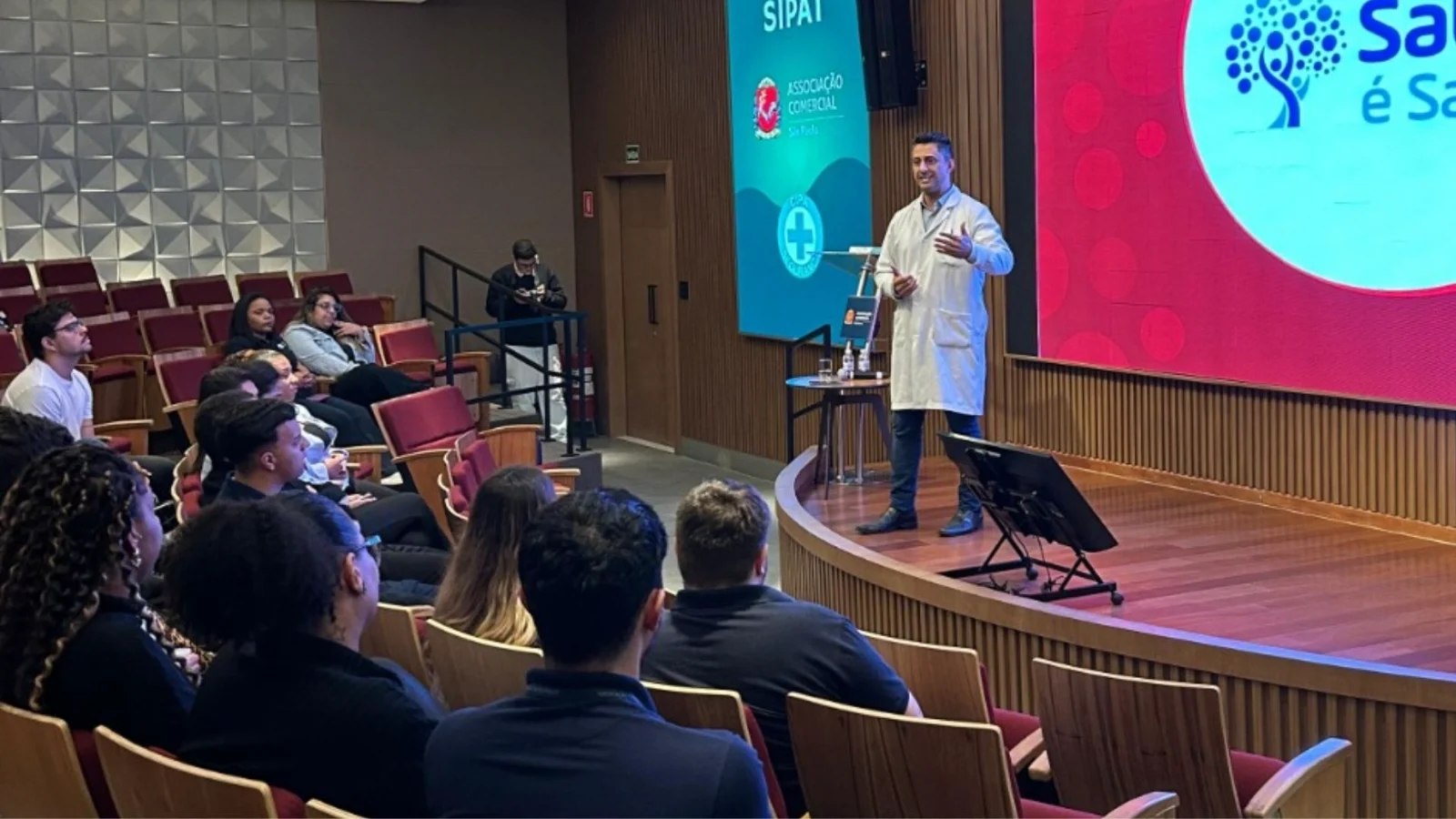 Palestra sobre saúde e bem-estar realizada em auditório, com participantes acompanhando a apresentação. A imagem representa o início de uma jornada de conscientização e incentivo à saúde corporativa.